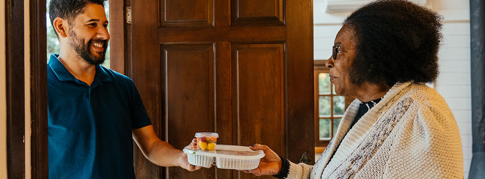 Volunteer handing meal to senior woman at her door