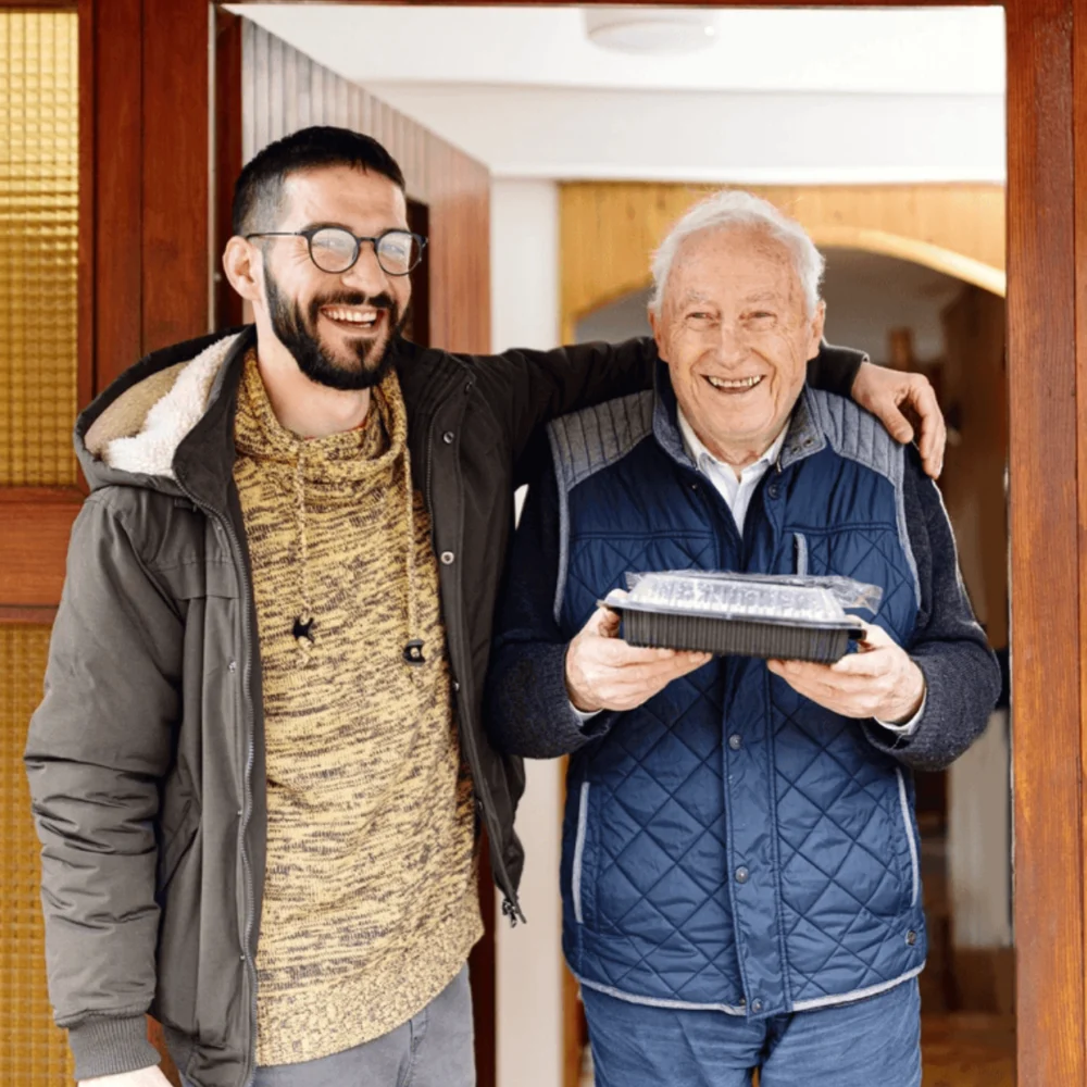 Male volunteer with elderly man at door with meal in hand